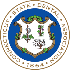The image shows a circular logo with text around its perimeter. In the center, there s a stylized map of Connecticut with the state s name above it. Below the map,  STATE DENTAL ASSOCIATION  is written in capital letters. At the bottom, the text reads  CONNECTICUT STATE DENTAL ASSOCIATION.  The logo has a blue background with a gold border and features a graphic of a tree and some leaves to the right.